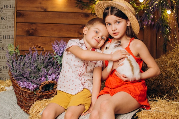bambini piccoli in fattoria con un coniglio su uno sfondo di fieno