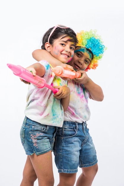 Bambini piccoli indiani o amici o fratelli che celebrano il festival di Holi con gulal o color polvere, dolci, pichkari o spray, isolati su sfondo bianco