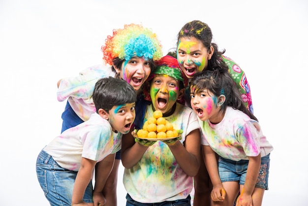 Bambini piccoli indiani o amici o fratelli che celebrano il festival di Holi con gulal o color polvere, dolci, pichkari o spray, isolati su sfondo bianco