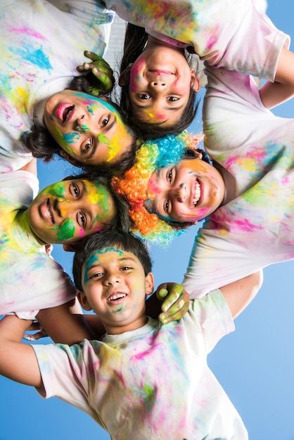 Bambini piccoli indiani o amici o fratelli che celebrano il festival di Holi con gulal o color polvere, dolci, pichkari o spray, isolati su sfondo bianco