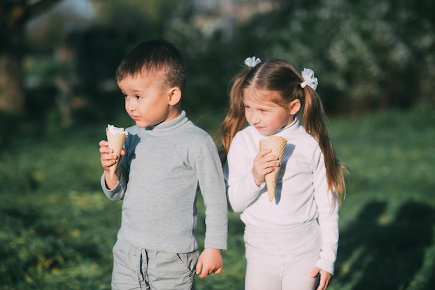 Bambini Ragazzo e ragazza che mangiano il gelato all'aperto su erba e alberi sullo sfondo molto dolci