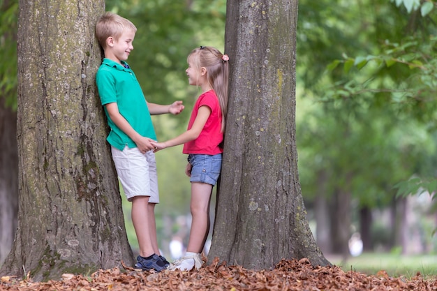 Bambini ragazzo e ragazza che stanno vicino al grande tronco di albero nel parco di estate