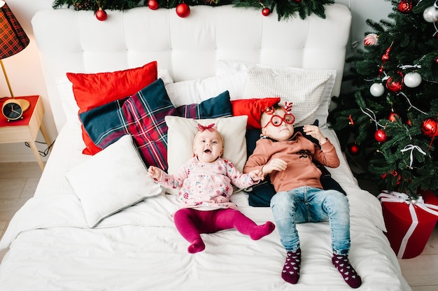 Bambini Ragazzo ragazza o figlio e figlia sul letto vicino all'albero di Natale Felice Anno Nuovo e Buon Natale