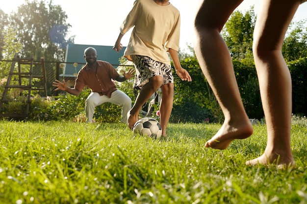 Bambini scalzi e il loro padre giocano insieme a calcio sul prato verde