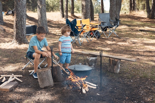 Bambini seduti intorno a un falò nella foresta in estate Picnic in famiglia all'aperto Vita da campeggio Cucinare nel calderone in fiamme nella natura