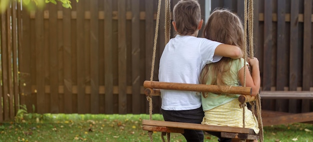 Bambini seduti su un'altalena in giardino fratello maggiore che abbraccia la sorellina