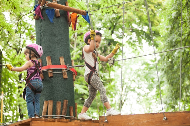 Bambini sulla corsa ad ostacoli nel parco avventura in casco da montagna e equipaggiamento di sicurezza