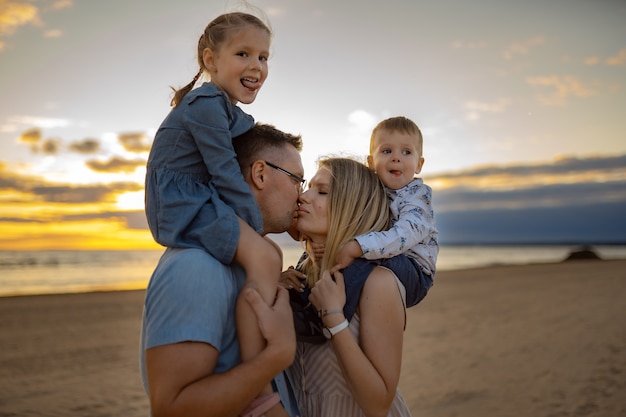 bambini sulle spalle dei genitori sulla spiaggia al tramonto mamma e papà che baciano il concetto di vacanza in famiglia