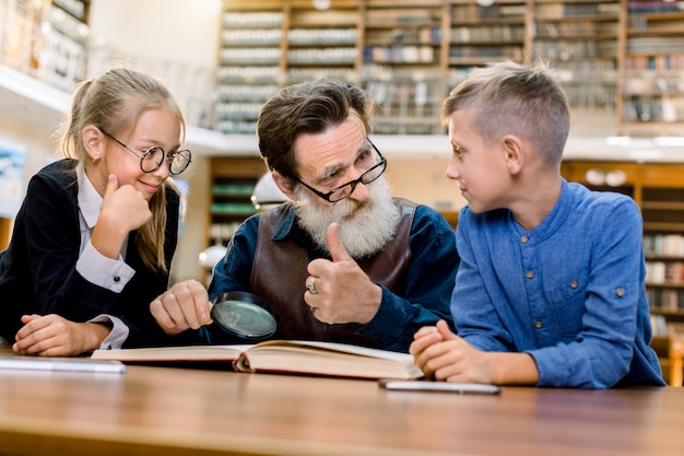 Bambini teenager sorridenti felici con il libro di storia della lettura del nonno alla biblioteca d'annata