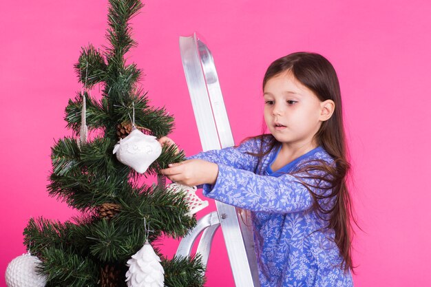 Bambini, vacanze e concetto di natale - bambina che decora l'albero di Natale su sfondo rosa