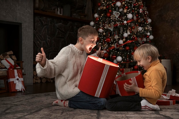 Bambini vicino all'albero di Natale con scatole regalo Due fratelli aprono con regali di Capodanno Bambini che aprono i regali di Natale