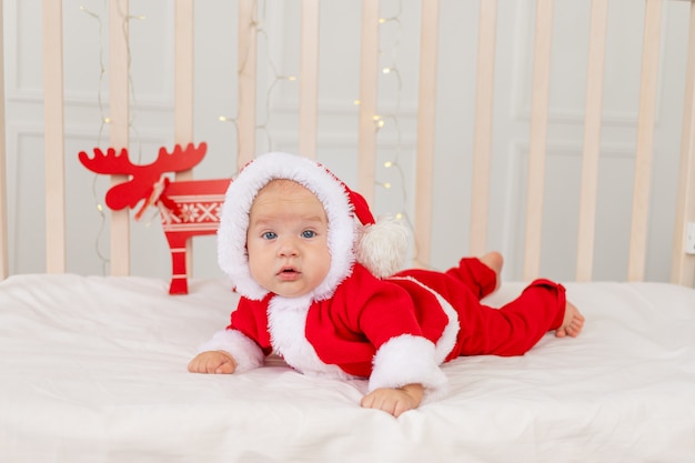 Bambino 6 mesi in un costume da Babbo Natale che giace in una culla a casa sul suo stomaco