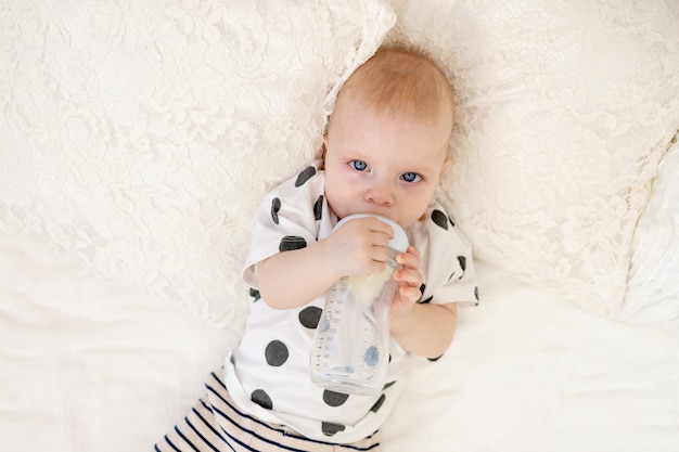 Bambino 8 mesi sdraiato sul letto in pigiama e bere latte da una bottiglia, concetto di pappe, vista dall'alto, posto per il testo