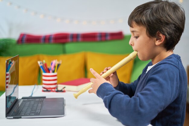 Bambino a casa che impara a suonare il flauto con un insegnante in linea connesso con il laptop