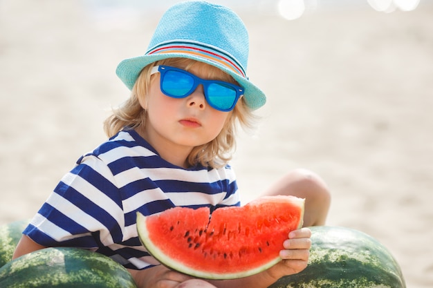 Bambino adorabile alla riva di mare che mangia anguria succosa. Bambino allegro in estate sulla spiaggia. Ragazzino sveglio all'aperto