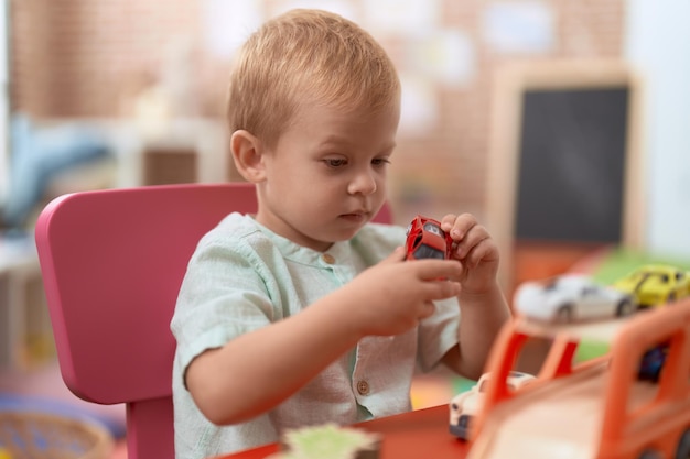 Bambino adorabile che gioca con il giocattolo dell'automobile che si siede sulla tavola all'asilo