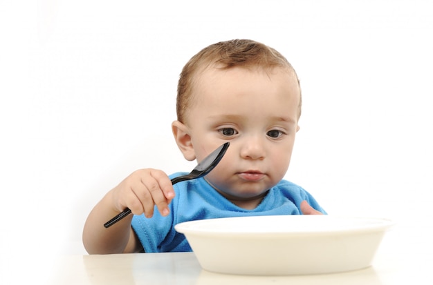 Bambino adorabile di un anno adorabile con gli occhi verdi che mangiano sul tavolo, sul cucchiaio e sul piatto