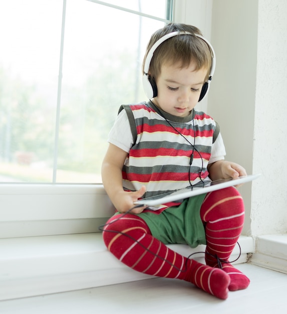 Bambino adorabile facendo uso della compressa e della cuffia avricolare a casa che ha tempo felice