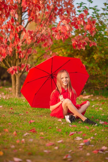 Bambino adorabile felice con l'ombrello rosso al giorno di autunno