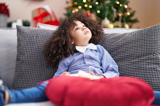 Bambino afroamericano che gioca con il giocattolo dell'automobile che si siede sul pavimento vicino all'albero di natale a casa