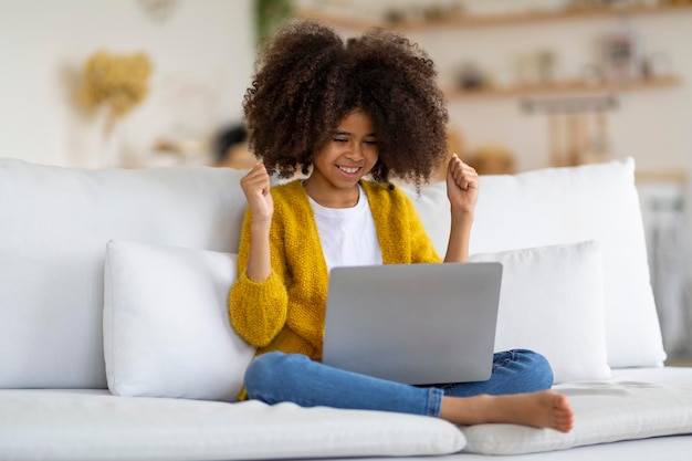 Bambino afroamericano emotivo che usa il computer portatile che alza i pugni