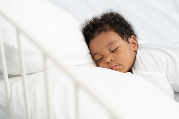 Bambino afroamericano nero che dorme su un materasso bianco.