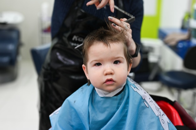 Bambino al primo piano parrucchiere. Il primo taglio di capelli del bambino dal parrucchiere. Taglio di capelli del bambino.