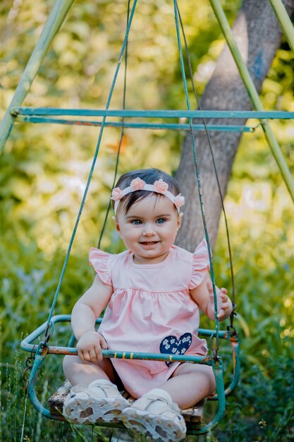 Bambino alla moda con vestito viola che si siede sul sedile dell'altalena nel parco