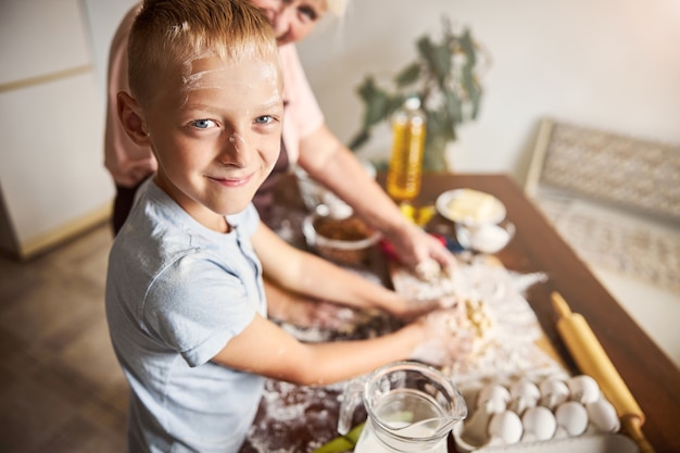 Bambino allegro che si diverte in cucina con la sua gentile nonna