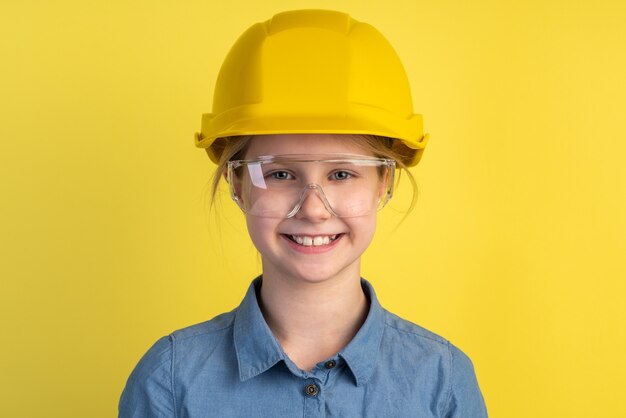 Bambino allegro e sorridente in un casco e occhiali da costruzione su una parete gialla