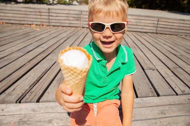 Bambino allegro in occhiali da sole che mostra il cono gelato