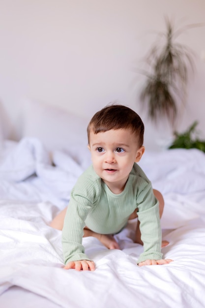 Bambino allegro in un body di cotone verde è sdraiato a pancia in giù su un letto bianco Foto di alta qualità