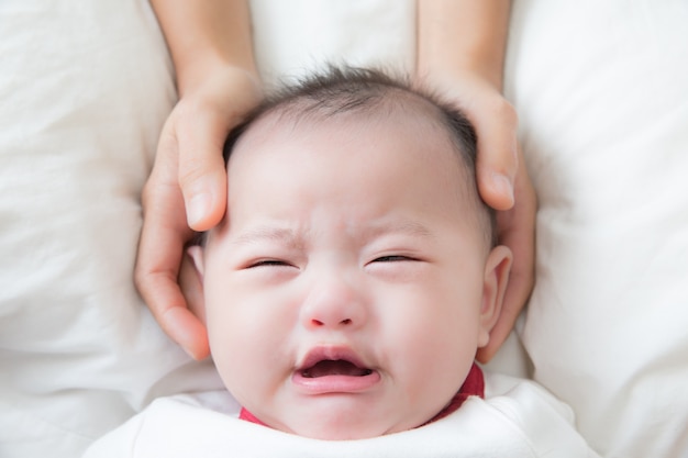 Bambino asiatico che piange sul letto bianco