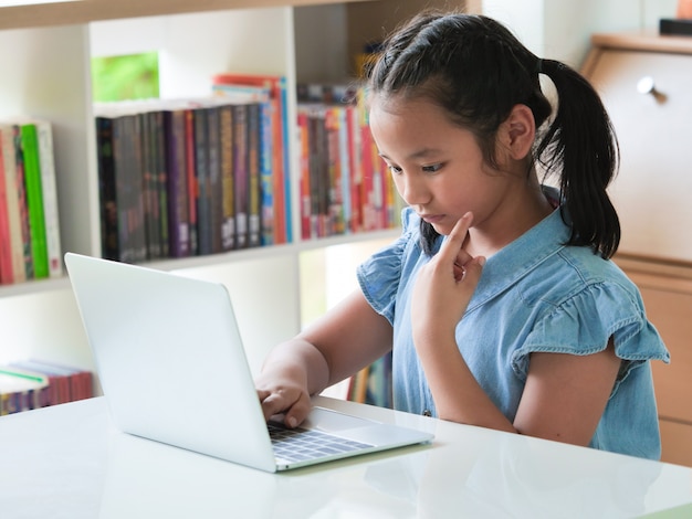 Bambino asiatico che utilizza computer portatile nella stanza delle biblioteche.