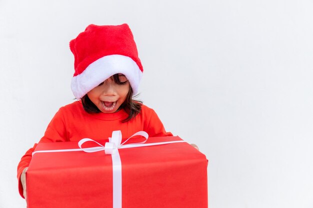 Bambino asiatico felice in cappello rosso della Santa che tiene i regali di Natale. Natale time.on sfondo bianco.