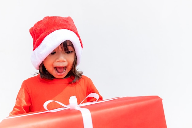 Bambino asiatico felice in cappello rosso della Santa che tiene i regali di Natale. Natale time.on sfondo bianco.