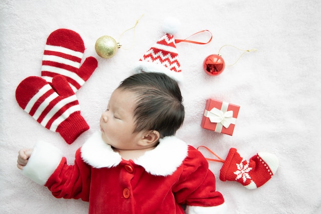 Bambino asiatico neonato sull'uniforme del Babbo Natale che dorme con il presente della scatola rossa e il cappello rosso