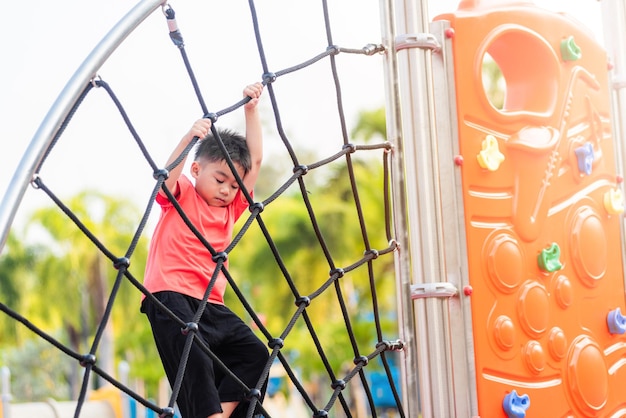 Bambino asiatico sorridente giocando arrampicata parco giochi all'aperto bambino in età prescolare felice divertendosi