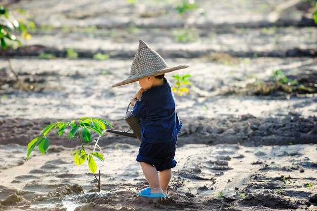 Bambino asiatico sveglio che innaffia giovane albero