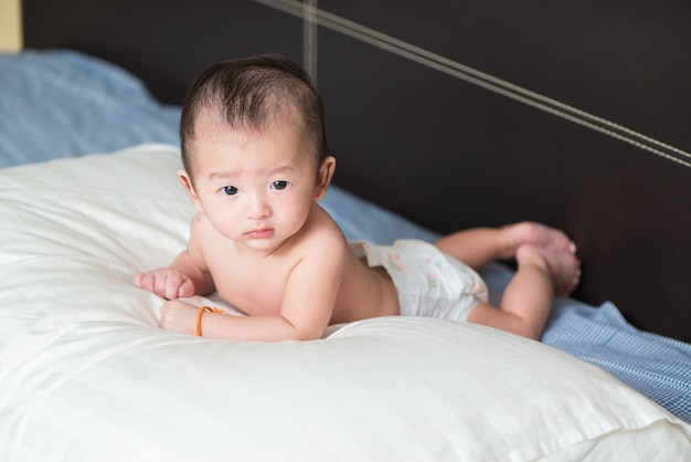 Bambino asiatico sveglio che si trova su un cuscino bianco