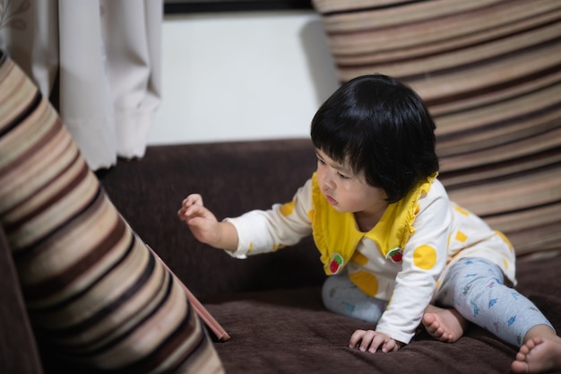 Bambino asiatico sveglio guardando il telefono cellulare e seduto sul divano