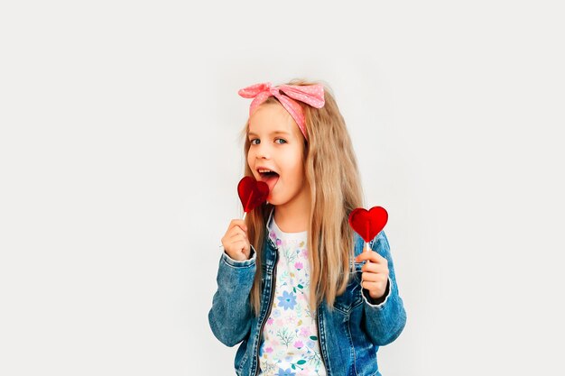 Bambino, bambina in possesso di caramelle a forma di cuore, isolato su sfondo bianco.