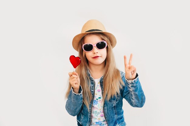 Bambino, bambina in possesso di caramelle a forma di cuore, isolato su sfondo bianco.