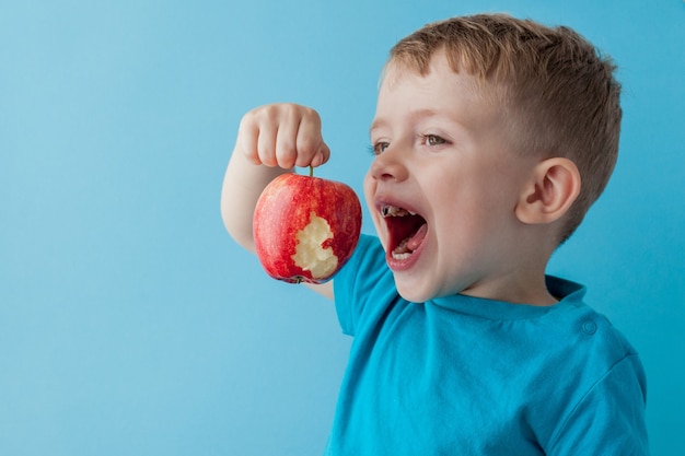 Bambino bambino che tiene e mangia mela rossa su sfondo blu