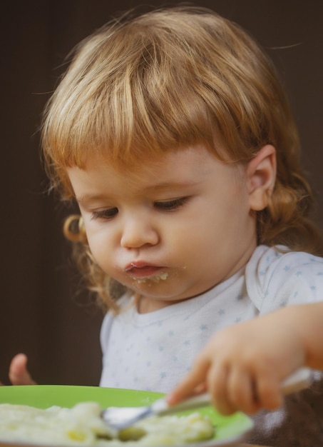 Bambino bambino con un cucchiaio e un piatto in cucina a casa