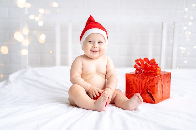 bambino bambino in rosso santa berretto si siede con un regalo su uno sfondo bianco capodanno vacanze di natale