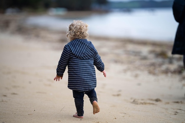 bambino biondo della ragazza che esplora sulla sabbia sulla spiaggia