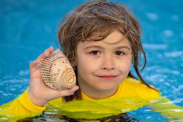 Bambino biondo divertente ritratto estivo bambino tenere conchiglia in mare bambino felice che gioca in acqua in estate mare s