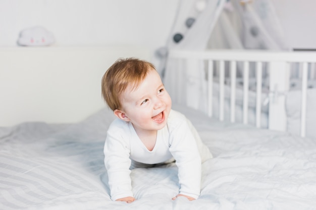 Bambino biondo sveglio in letto bianco