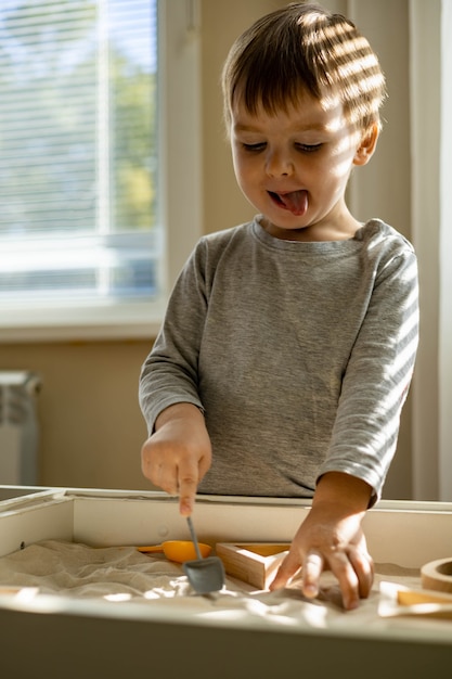 Bambino carino che gioca a sandbox cinetico domestico per lo sviluppo personale usa il metodo maria montessori